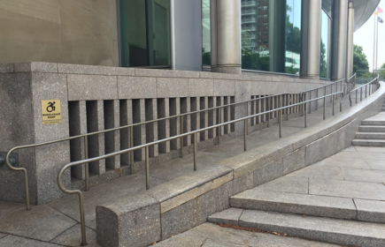 A long ramp leading to the entrance. There are steps to the right of the ramp leading in the same direction. To the left of the ramp on the side of the building is ADA signage.