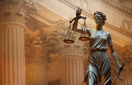 Statue of Lady Justice wearing a blindfold, holding scales and a sword, with ornate courthouse columns in the background