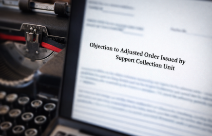 A photo with part of a typewriter on the left and a screen with objection to adjusted order issued by support collection unit visible. All other text is blurred.