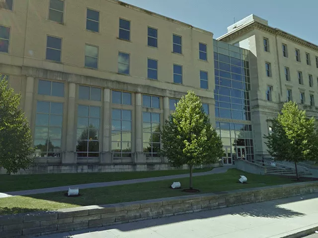 An angled view of the courthouse. There is a walkway between two grassy areas that leads to the entrance. There are stairs that lead directly to the entrance from the sidewalk.