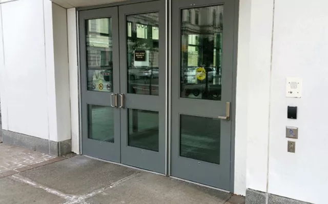 A set of double doors to the left and a single door to the right. The single door is automatic and the push button is located to the left of the door and is directly attached to the wall.