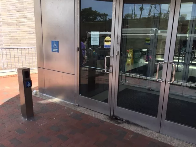 A single door with a set of double doors to the right. The entrance is accessed on street level. There is a pole with a push button on the sidewalk toward the left-hand side.