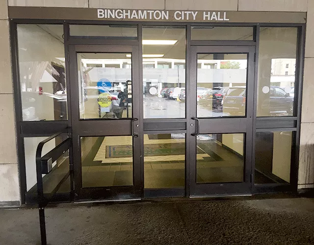 Description of photo: There are two single doors located at the entrance to Binghamton City Hall. There is a push button located on a railing to the left that can be pushed to open the left door.