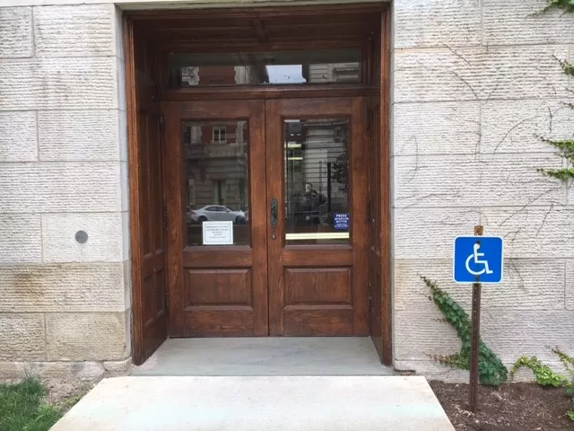 Description of photo: There are two wooden doors at the end of the walkway. There is a blue ADA-accessible sign to the right in the garden area.