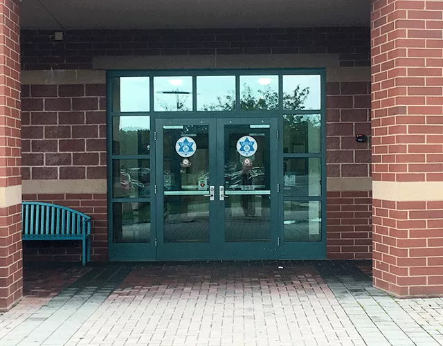 ADA-accessible entrance with signage. The double doors are accessed from the street level. To the left of the doors is a bench.