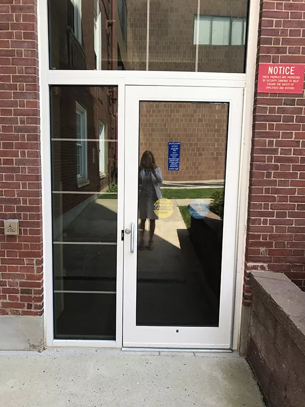 Description of photo: The entrance is a single white door. There is a push button to open the door to the left of the door.
