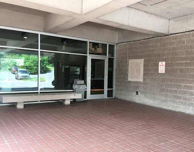 Description of photo: The courthouse has a single door to the right. On the left is a garbage pail and a bench.