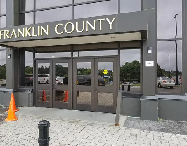 Description of photo: The courthouse has two sets of double doors on street level. The set to the right has a sign that it is automatic. There are two orange cones to the side of the left set of doors.