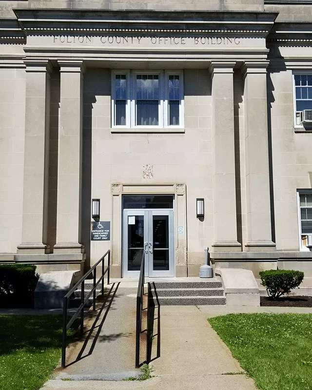 Description of photo: A walkway that leads to a ramp on the left and steps to the right. Ahead of both the ramp and stairs is a set of double doors.   