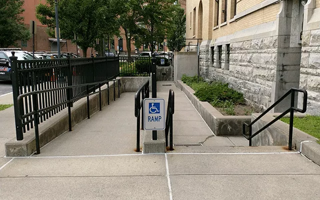 Description of photo: A walkway that leads to a ramp on the left and down the steps to the right. The entrance to the court facility is on the far right.