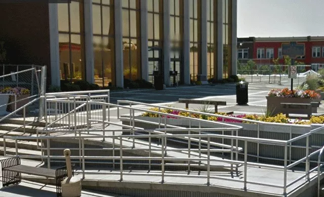 Description of photo: A winding ramp and stairs that lead to an open area. The entrance to the facility is located on the far right.