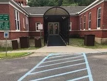 Description of photo: A crosswalk from the parking area leading to a ramped entry way. The double door entrance is accessed directly from the ramp.