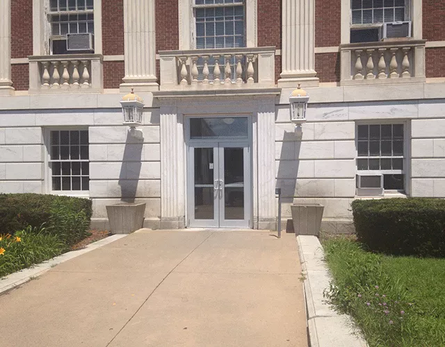 Description of photo: The double door entrance that is accessed from a walkway. There is a push button on a pole to the right of the doors.