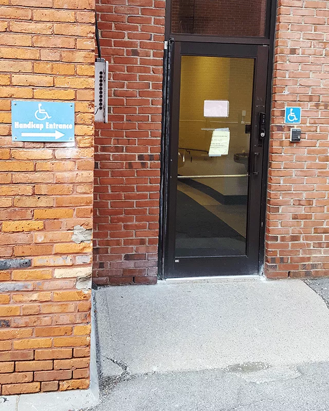  A single door that has ADA-accessible signage both to the left and right of the door. There is a bell located under the signage to the right hand side of the door.
