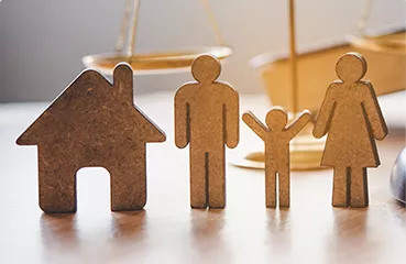 symbolic wooden figures representing a family and a house placed in front of the scales of justice
