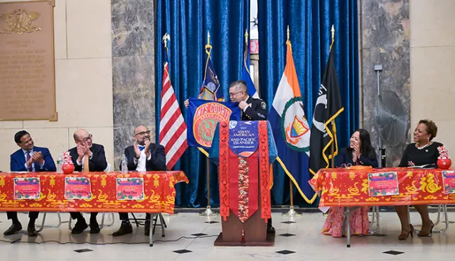 Major and New York State Courts’ Asian Jade Society President Henry Chen presents the Society’s flag during the colorful Bronx program. Sitting on the dais are (L-R) Staten Island’s Supervising Judge of Criminal Courts Biju Koshy, retired Appellate Division Associate Justice Jeffrey Oing, New York City Civil Court Administrative Judge Shahabuddeen Ally, Bronx County Family Court Judge Karen M.C. Cortes, and New York City Family Court Administrative Judge Anne-Marie Jolly 