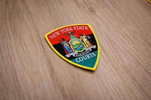The New York State Courts’ newly launched commemorative patch for Black History Month mirrors the standard Court Officer’s patch, replacing the dark blue background with the Pan-African colors of red, black, and green. 