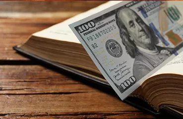 Photo of an open book with a hundred dollar bill stuck in it.