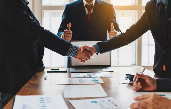 Two professionals shaking hands, and one giving thumbs up behind them