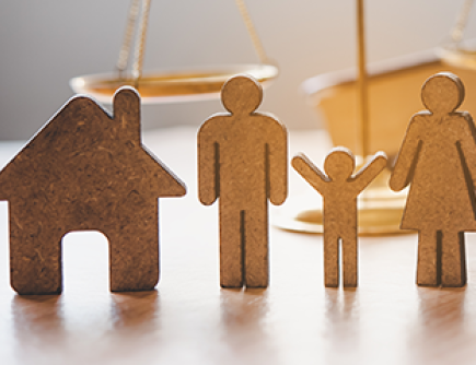 symbolic wooden figures representing a family and a house placed in front of the scales of justice